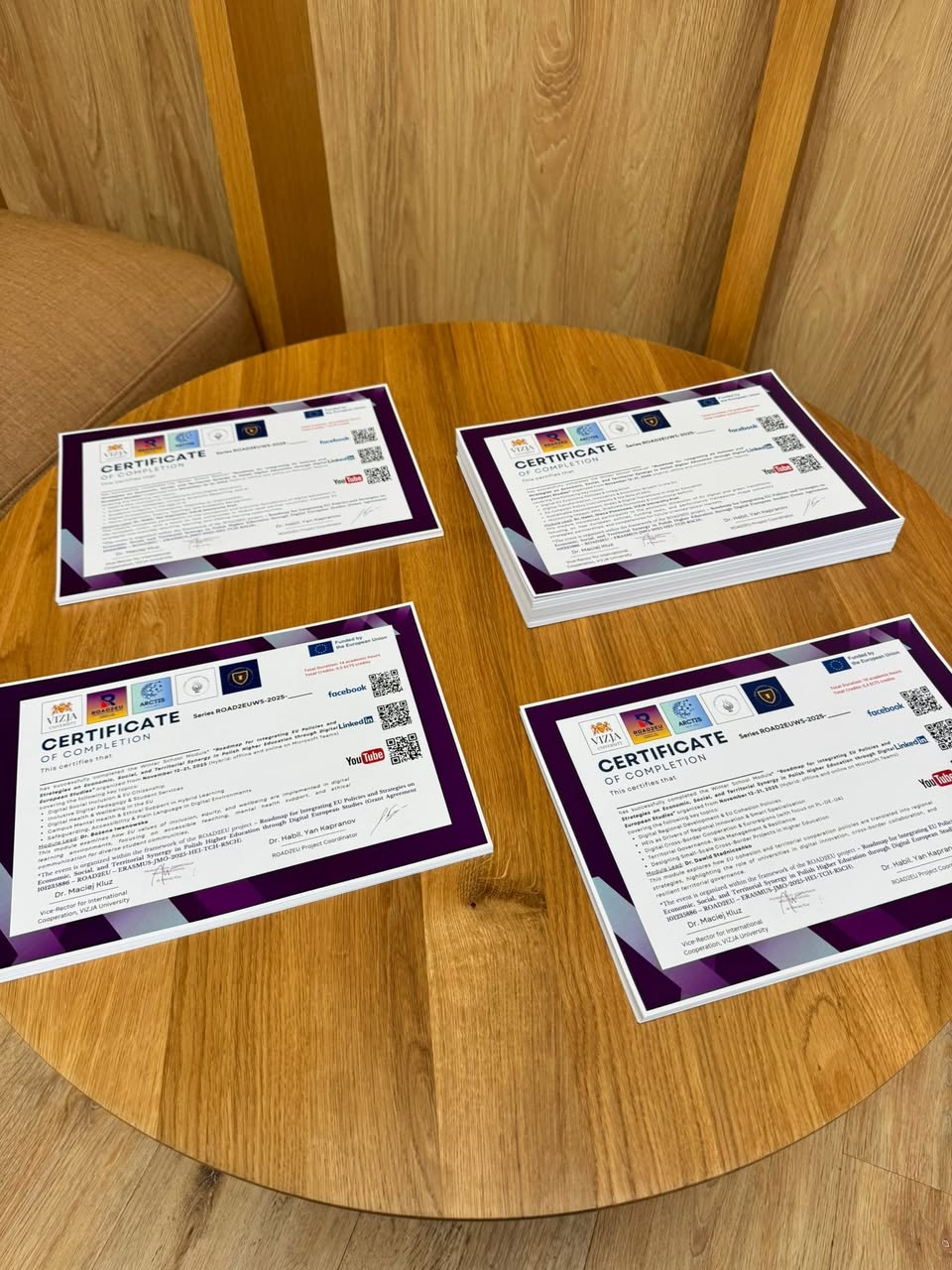 Prepared ROAD2EU Winter School 2025 participant certificates displayed on a table.
